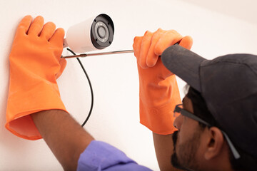 Shoulder shot of Electric Technician man setup cctv camera security system on wall - Electrician installing video surveillance camera - obrazy, fototapety, plakaty