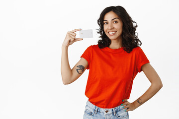 Stylish modern girls shows credit card, smiles satisfied, recommends bank, shopping days in store, buying something contactless, standing over white background