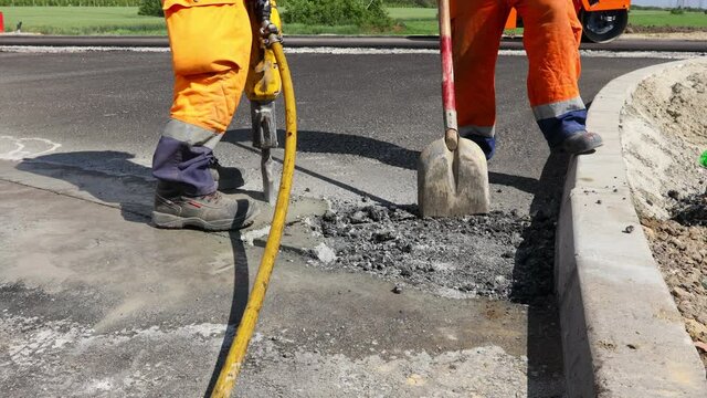 Construction worker breaks asphalt with a pneumatic jackhammer. Man using shovel to pick up and throw away cracked parts.