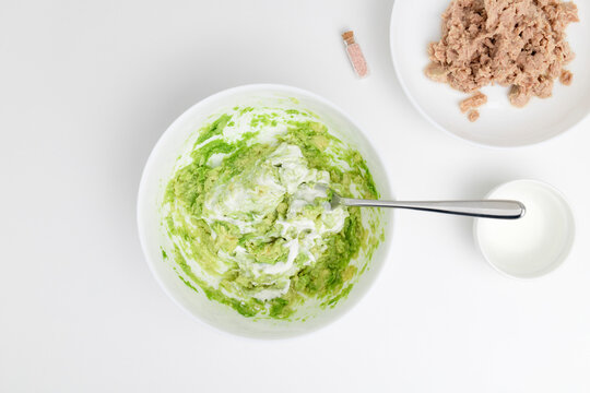 Stirring The Mashed Avocado With Yogurt On The White Plate. Tuna And Spices Are On The Background. Step-by-step Recipe.