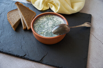 Summer cold yoghurt soup Okroshka. Vegetable soup made from radish and cucumber and green herbs. Traditional national dish, like in a restaurant on the table, a spoon lies on a plate