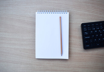 A blank notebook with pencil on wood desk background. Top view with copy space.