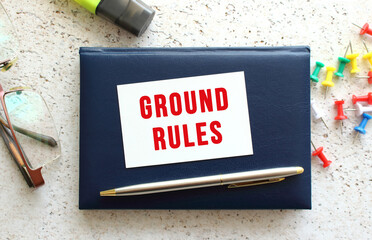 Text GROUND RULES on a business card lying on a blue notebook next to the glasses and stationery.
