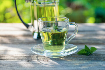 A cup with fresh scented mint tea on a wooden table in the summer garden.