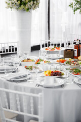 
Beautifully set table in the banquet hall of the restaurant. A table with appetizers for wine, cold dishes and salads. White tablecloths and napkins
