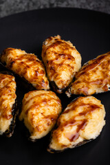 Oysters with cheese on a dark plate, grey background.
