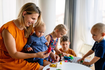 Mother or nursery teacher teaches her children to work with colorful play clay toys