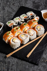 Set of different sushi rolls on a dark background. Sauce and chopsticks.