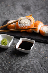 Set of fresh tasty sushi rolls with salmon and cheese. Chopsticks holding sushi on a dark background. Wasabi and soy.