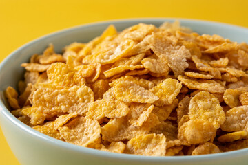 Corn flakes in a blue bowl on yellow background. Close up