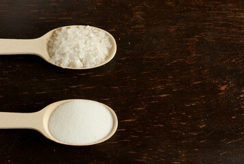 A spoonful of sea rock salt, a spoonful of extrasalt. Two wooden spoons with salt on the left on a dark wooden background. Coarse sea salt and small bulk salt