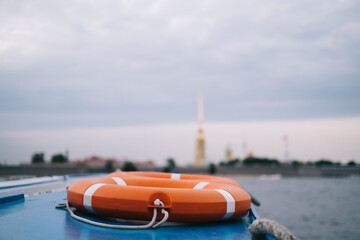 An orange lifebuoy on a pleasure boat, in the background the architecture of St. Petersburg, the...