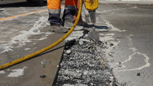 Construction worker breaks asphalt with a pneumatic jackhammer. Man using shovel to pick up and throw away cracked parts.