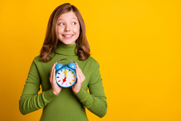 Photo portrait girl cheerful keeping alarm clock smiling looking copyspace isolated vivid yellow color background