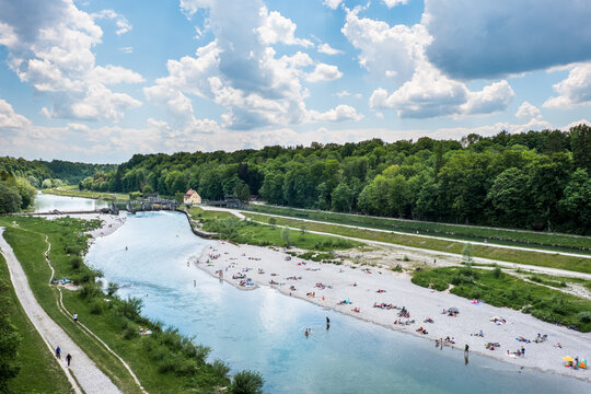 Blick auf die Isar von der Gro&szlig;hesseloher Br&uuml;cke bei M&uuml;nchen mit Menschen beim Baden im Fr&uuml;hling / Sommer an Kiesstrand