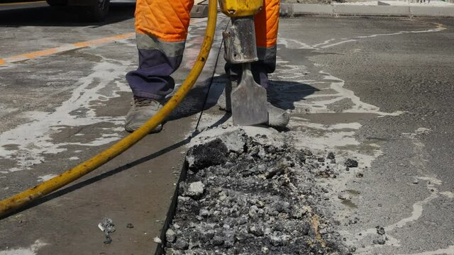 Construction worker breaks asphalt with a pneumatic jackhammer. Man using shovel to pick up and throw away cracked parts.