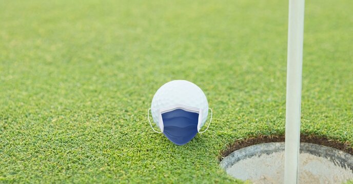 Composition of golf ball with face mask on grass with copy space