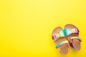 Colorful kid sandals on bright yellow table background. Closeup. Empty place for text. Top down view.