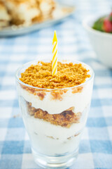 Russian honey cake in a glass with yellow candle on a blue tablecloth