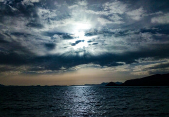Panoramic seascape and cloudscape sky with sun burst through white dramatic cloud, calm blue sea ,and mysterious island mountain landscape .