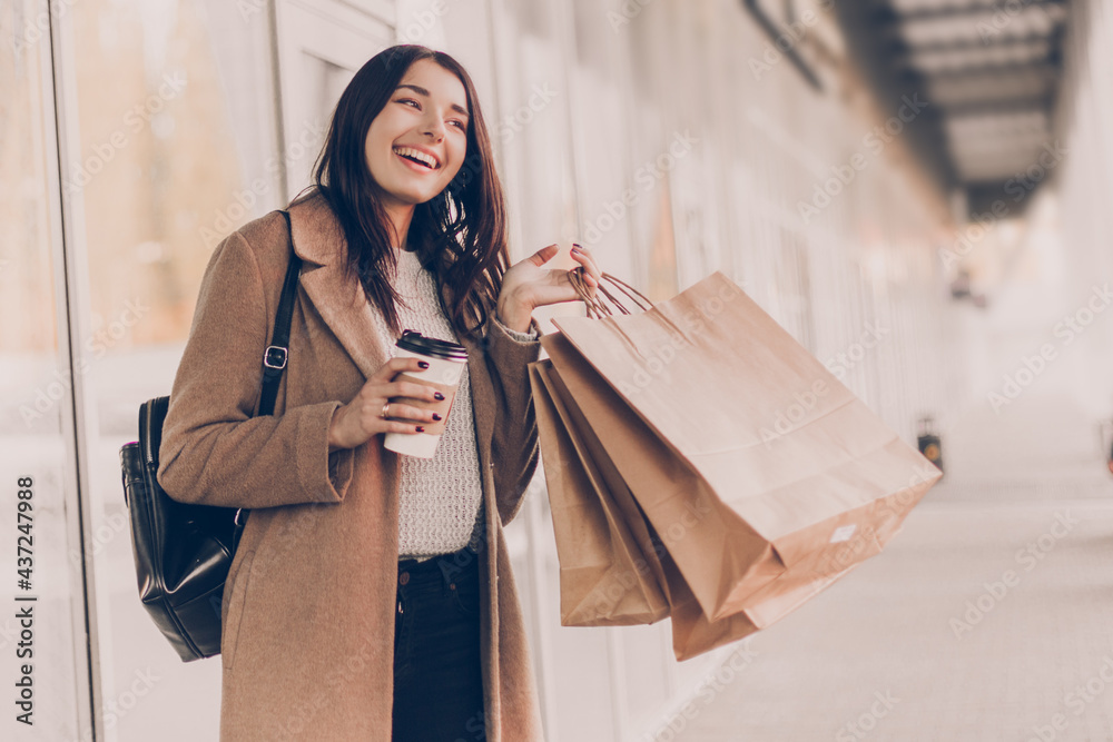 Wall mural beautiful smiling young woman with shopping bags and coffee on the street.