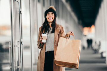 Young woman with shopping bags and coffee walking near mall.