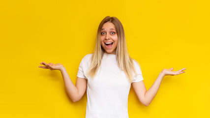 A young caucasian amazed pretty charming blonde woman in a white t-shirt smiles and spreads hands with doubt isolated on a bright color yellow background. Banner