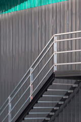 Side view of metal stairs and banister on gray and green corrugated steel wall of storehouse...