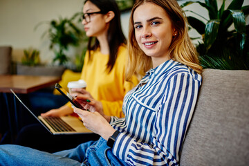 Cheerful female using smartphone while spending time with friend in cafe