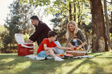Happy young mother and father with little boy smiling while having picnic outdoors