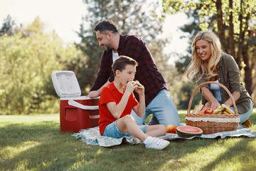 Happy young mother and father with little boy smiling while having picnic outdoors