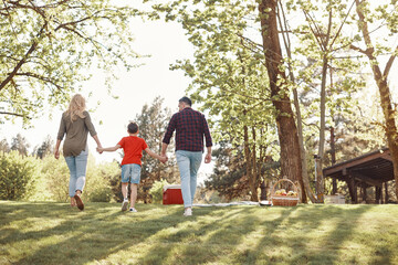 Naklejka premium Rear view of young mother and father with little boy holding hands and walking outdoors