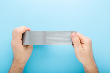 Young adult man hands stretching gray adhesive tape on light blue table background. Pastel color....