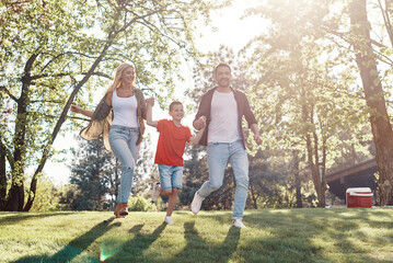 Obraz premium Happy young mother and father with little boy holding hands and walking outdoors