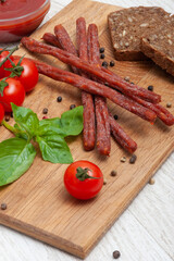 Thin sausages with tomatoes and herbs and black bread on a wooden board