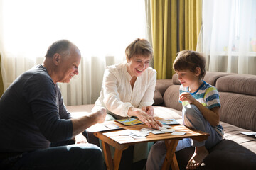 Fototapeta premium grandparents with grandson playing board game together at home. quarantine. Family having fun playing at home. Family board games. 
