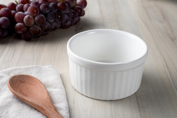 Empty white bowl on wooden desk. Grapes on background