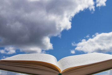  Blurry pages of an open book, on a background of blue sky with clouds.