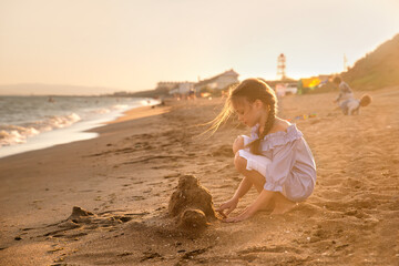 Portrait of beautiful little girl builds a sand castle in sunset