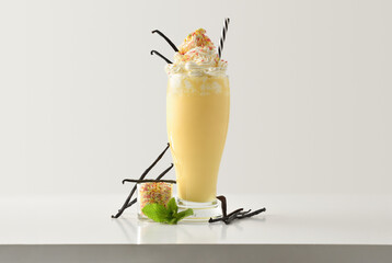 Vanilla milkshake with cream decorated with branch vanilla on table