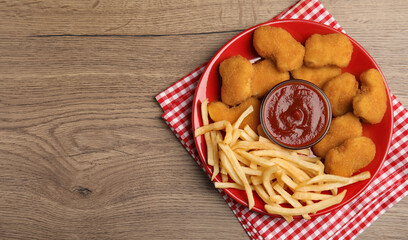 Tasty chicken nuggets and French fries served with ketchup on wooden table, top view. Space for text