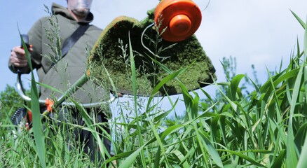 bottom view of a lawn mower in the hands of a worker with stuck cut grass, close-up of a manual...