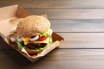 Delicious burger in cardboard box on wooden table. Space for text