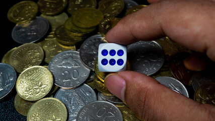 Hand holding a dice with a collection of gold and silver Malaysian 20 sen coin on background. © Aiman Khair