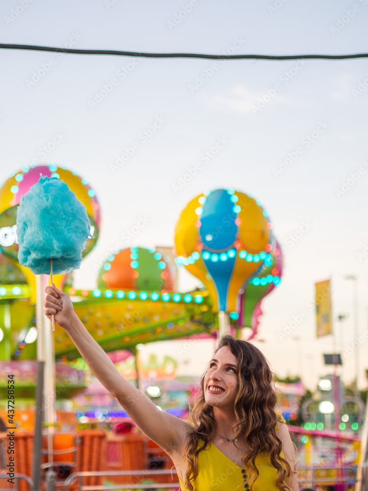 Wall mural Vertical shot of an attractive Caucasian female posing with blue cotton candy at a carnival