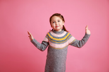 Portrait of little funny smiling girl in warm dress on rosa background