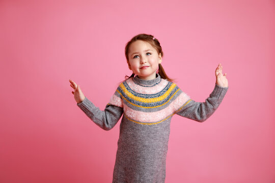 Portrait of little funny smiling girl in warm dress on rosa background