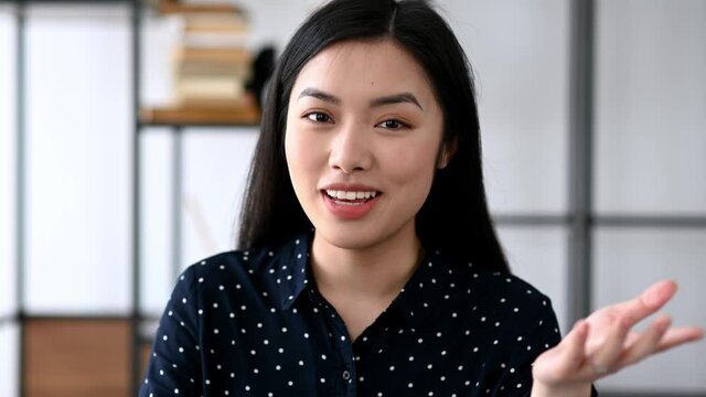 Distant communication. Friendly pretty smart confident young asian woman, freelancer or manager, sits at work desk, chatting with colleagues or friends via video call, waving hand, smiling