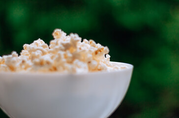 Fresh hot popcorn in a plate on the window.
Overlooking nature. Bokeh.
Side view. Copy space.
Place for text
