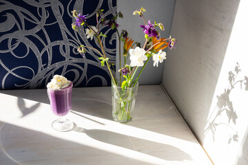 Blueberry milk shake with cream in cup, flowers in sun light on white and blue background